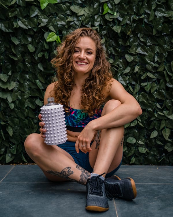 Lashara Wood, Level 3 personal trainer, sitting against a leafy wall in training kit with a water bottle